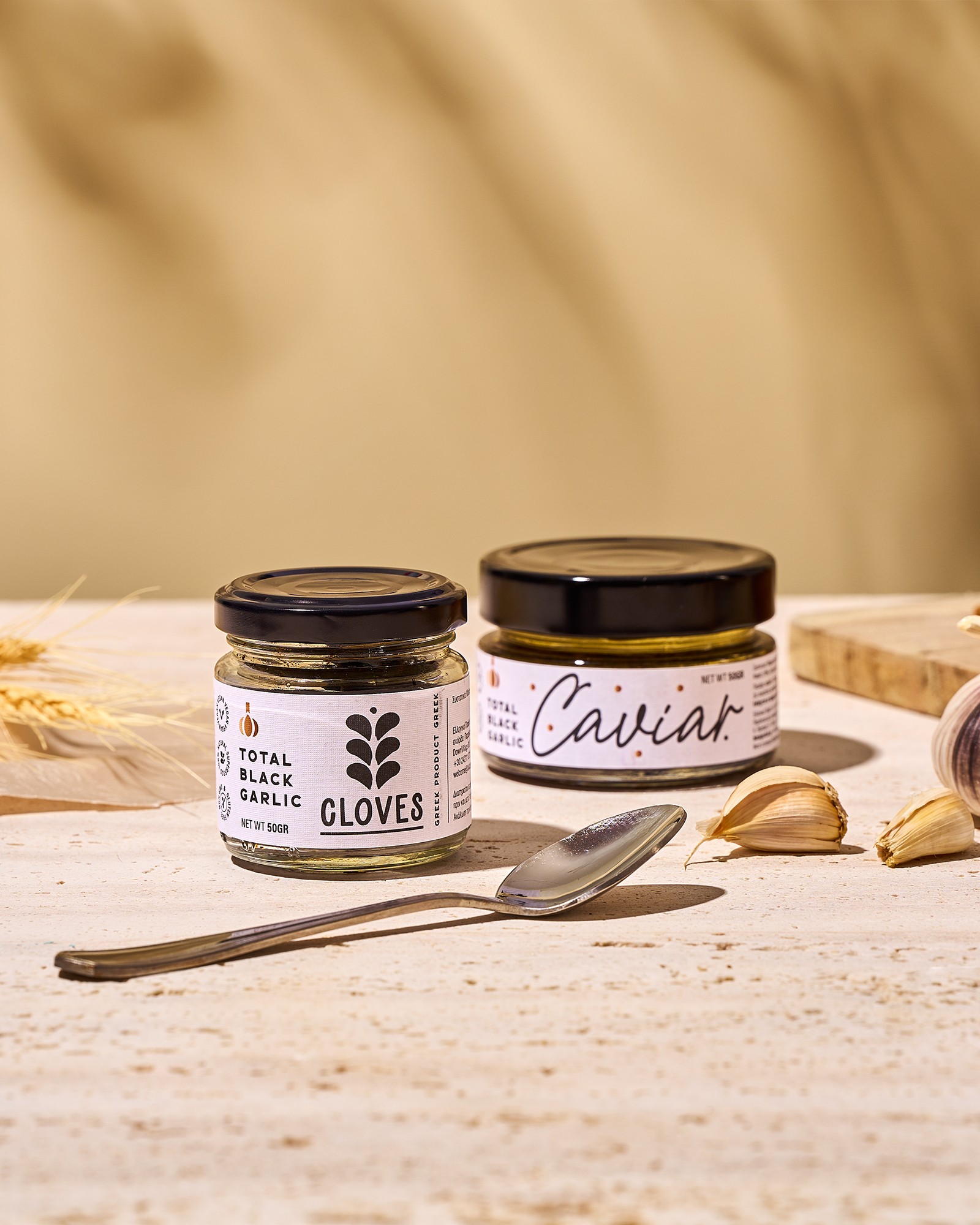 Total Black Garlic cloves and caviar jars with garlic and a spoon on a warm stone surface for Baransu