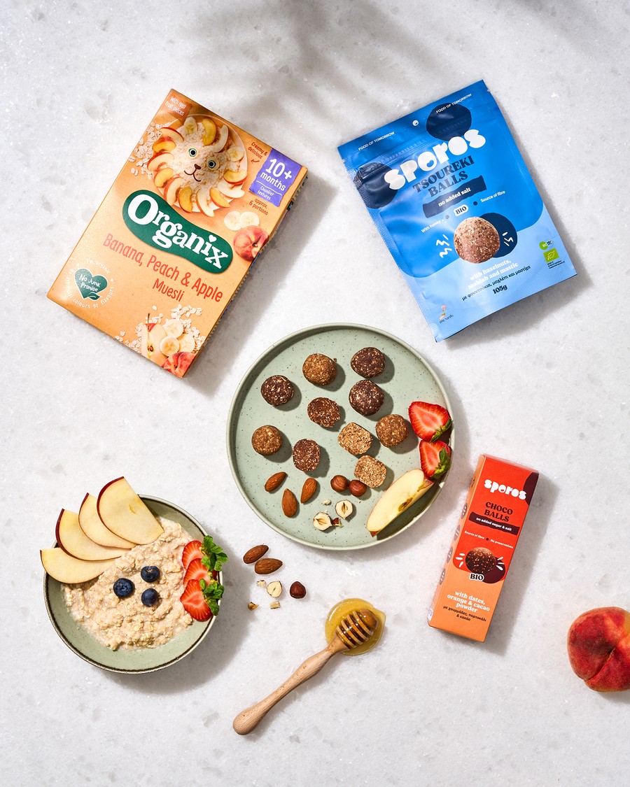 Baransu flatlay πρωινού με μούσλι Organix, συσκευασίες snacks Sporos, φρούτα και μπολ σερβιρίσματος