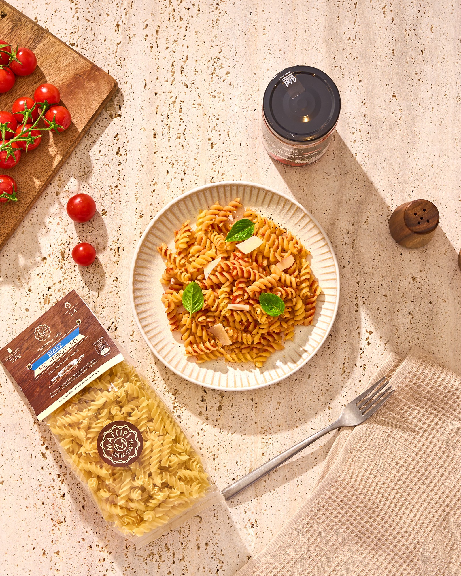 Fusilli pasta with basil and cheese beside pasta packaging, cherry tomatoes and a sauce jar, photographed for Baransu