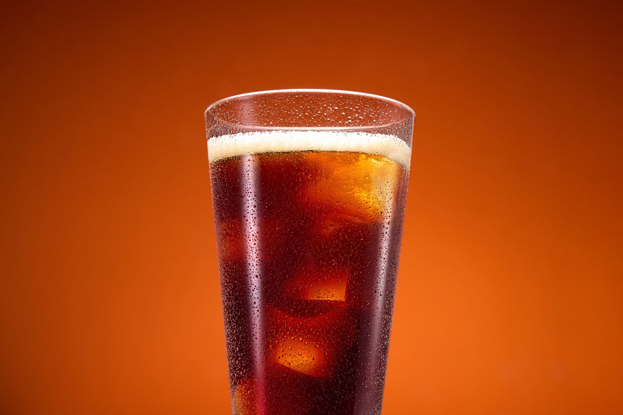 Dark soda glass with ice on orange backdrop