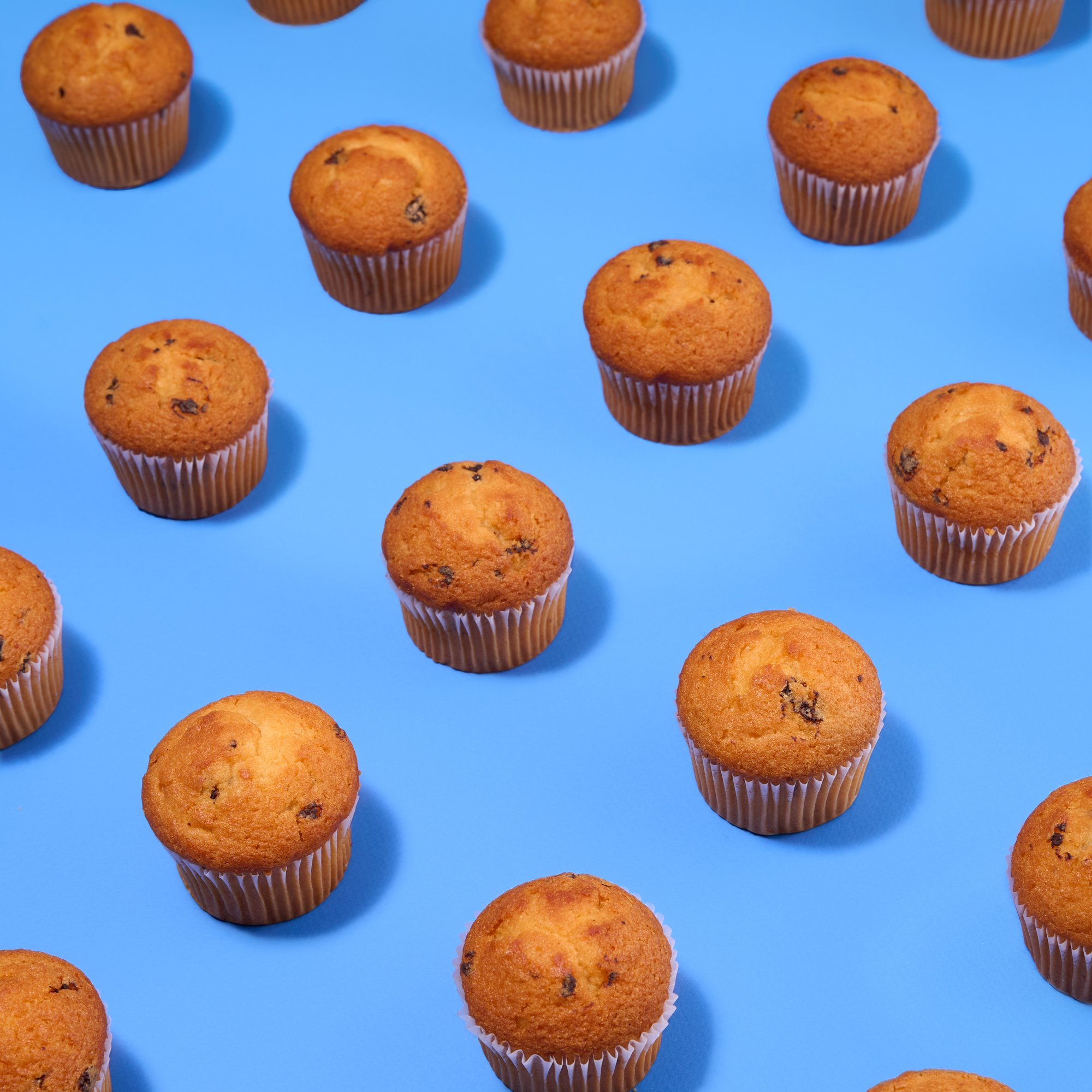 Chocolate-chip muffins on blue in a repeating pattern