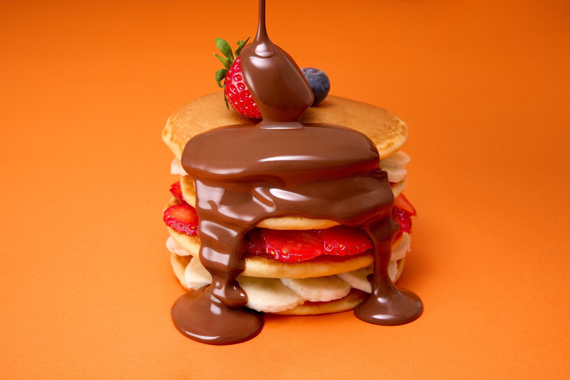 Pancake stack with chocolate drip and berries on orange