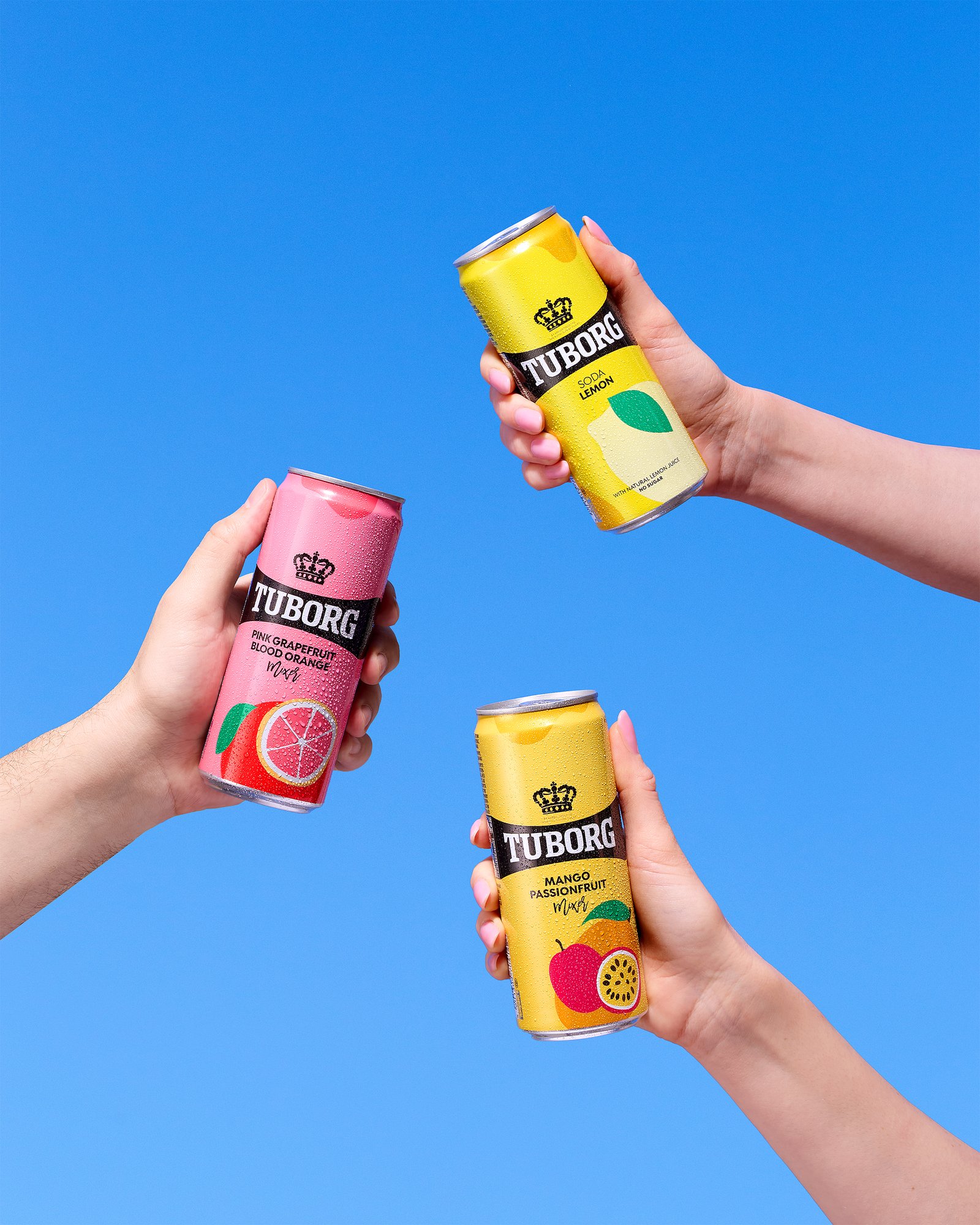 Hands holding Tuborg soda cans on blue sky