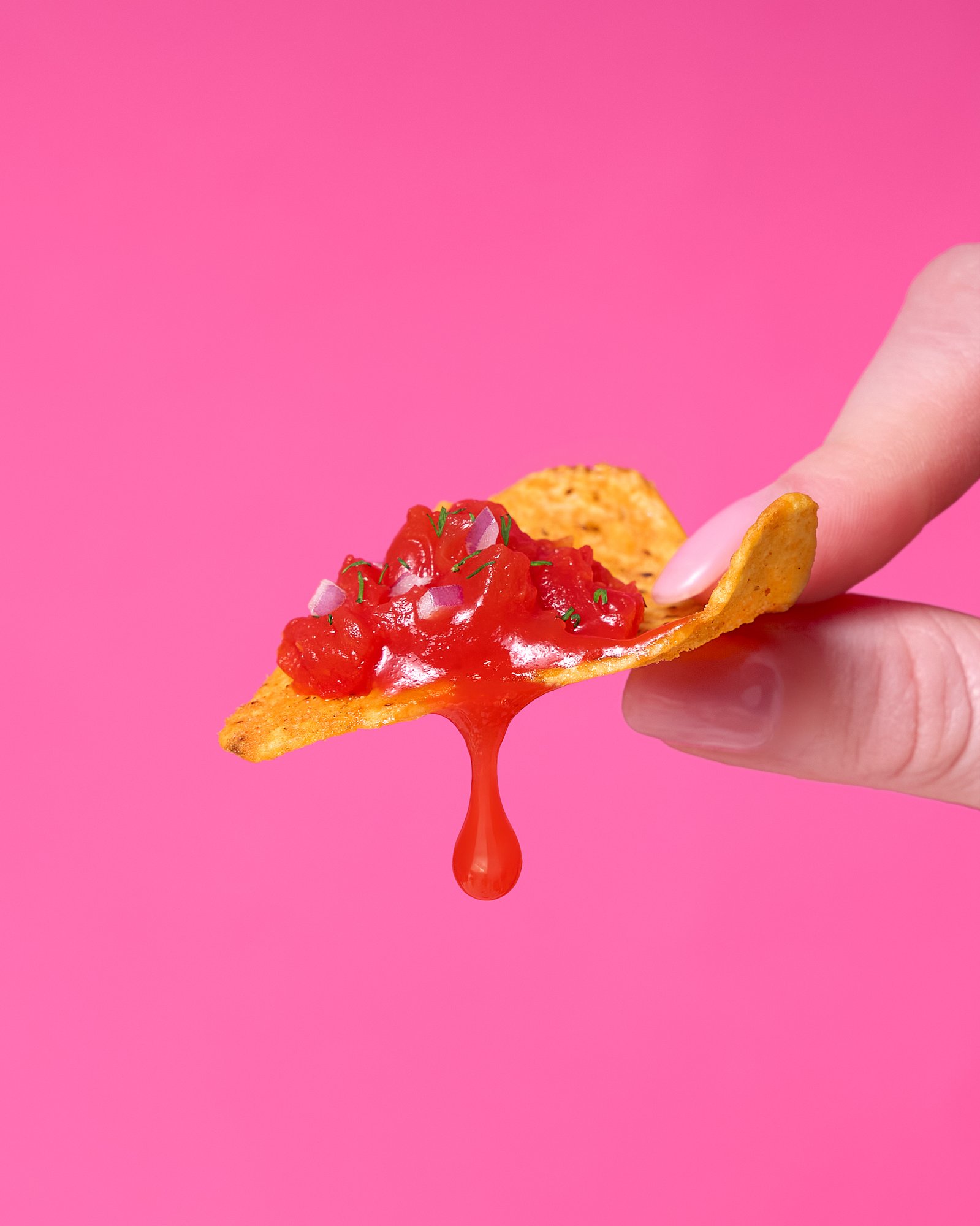 Tortilla chip with salsa drip on pink