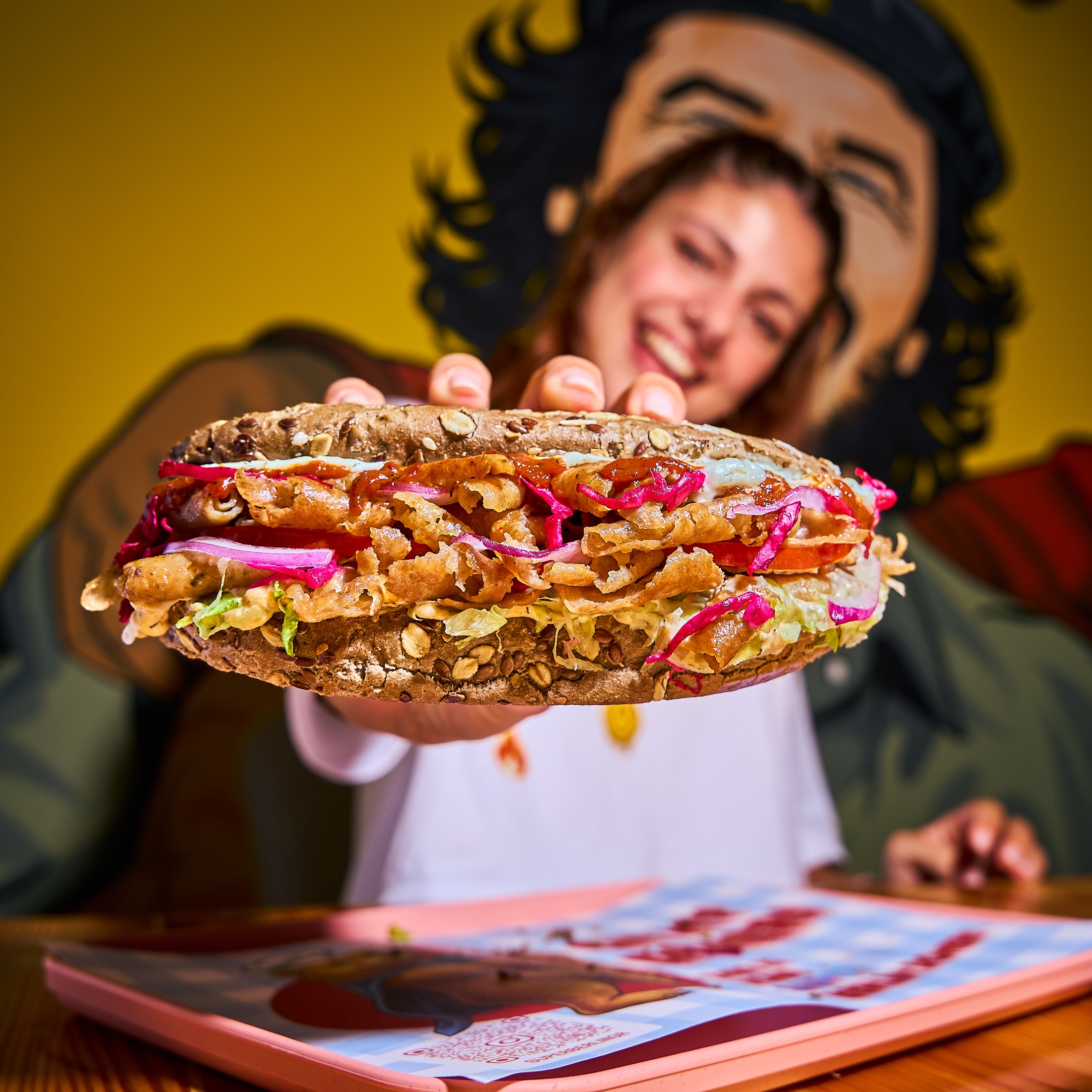 Woman offering a Super Berlin Doner sandwich toward the camera with her face softly out of focus